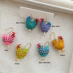 Colorful beaded chicken-shaped earrings on a beige fabric background