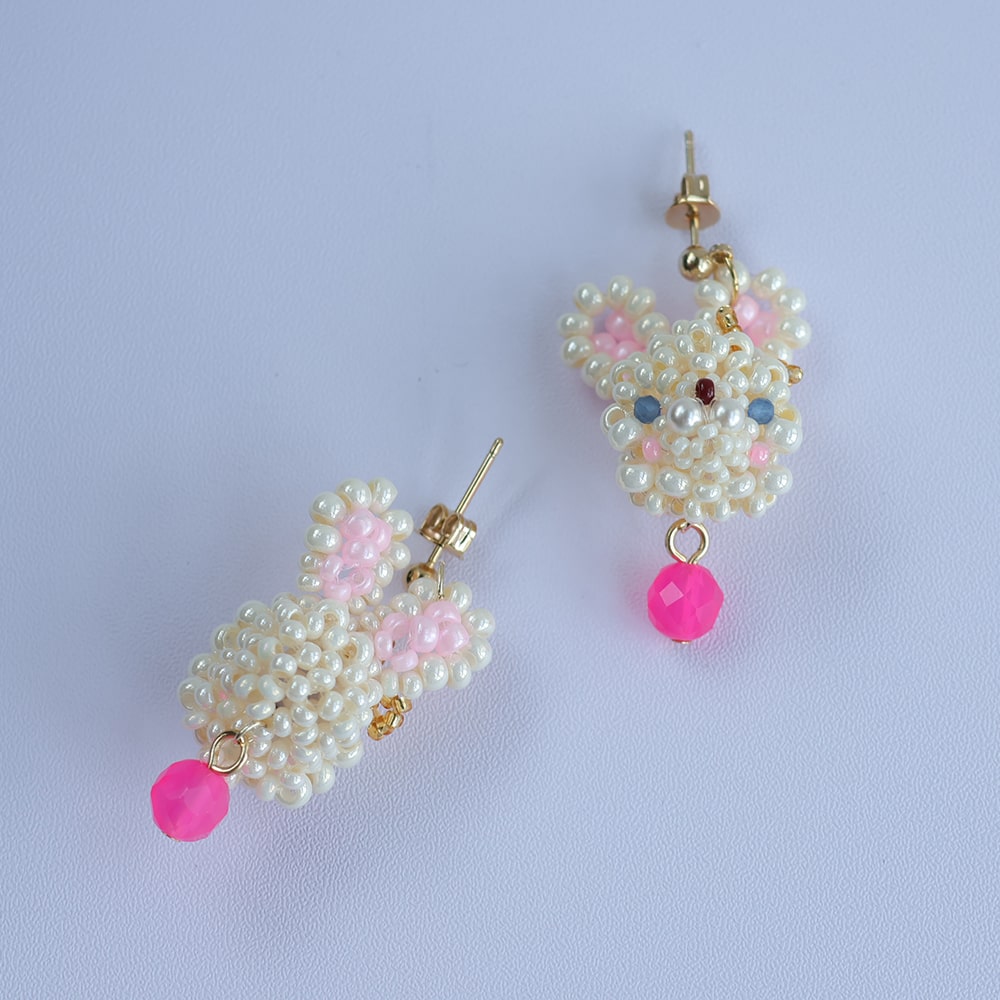 Pair of beaded earrings with pink accents on a light purple background