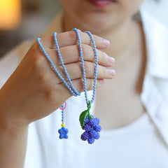 Hand holding a colorful beaded grape necklace with decorative elements against a blurred background