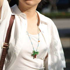 Person wearing a white shirt with a coconut necklace and a brown strap over their shoulder.