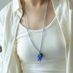 Person wearing a white top and a necklace with a grape pendant