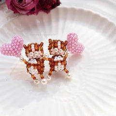 Pair of beaded animal earrings with pink hearts on a white surface.