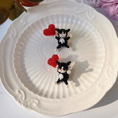 Two black cat-shaped earrings with red hearts on a white decorative plate.