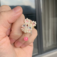 Hand holding a decorative ring with pearls and colorful beads against a blurred background
