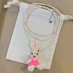 Beaded bunny necklace with pink dress on a white drawstring bag against a beige background