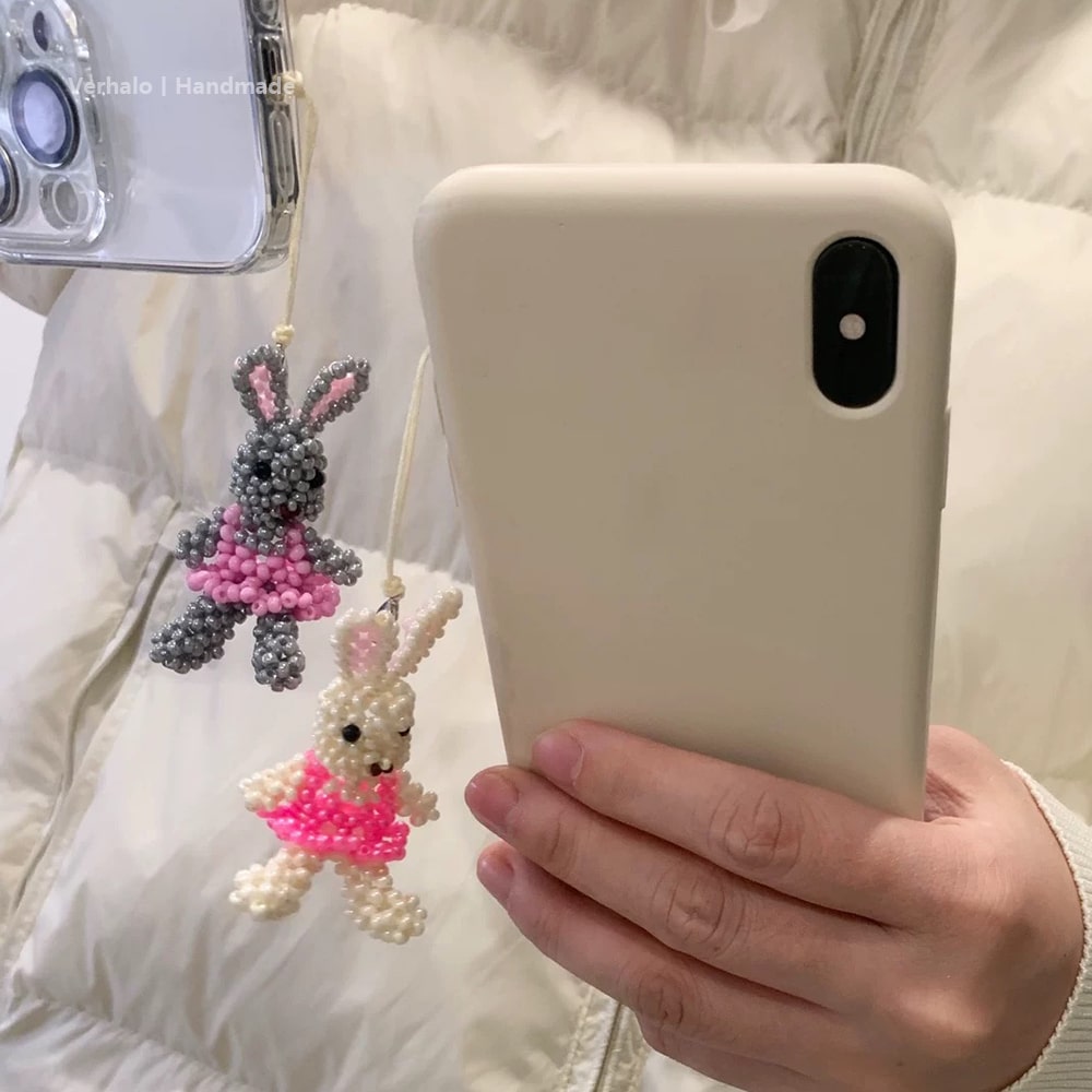 Person holding a phone with a white case, next to two beaded bunny charms.