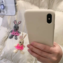 Person holding a phone with a white case, next to two beaded bunny charms.