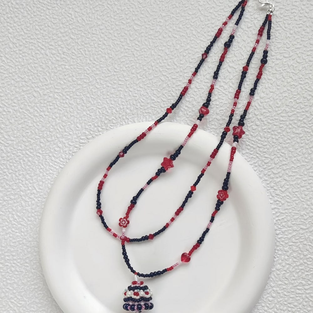 Beaded necklace with red and black beads on a white plate against a light gray background