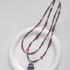 Beaded necklace with red and black beads on a white plate against a light gray background