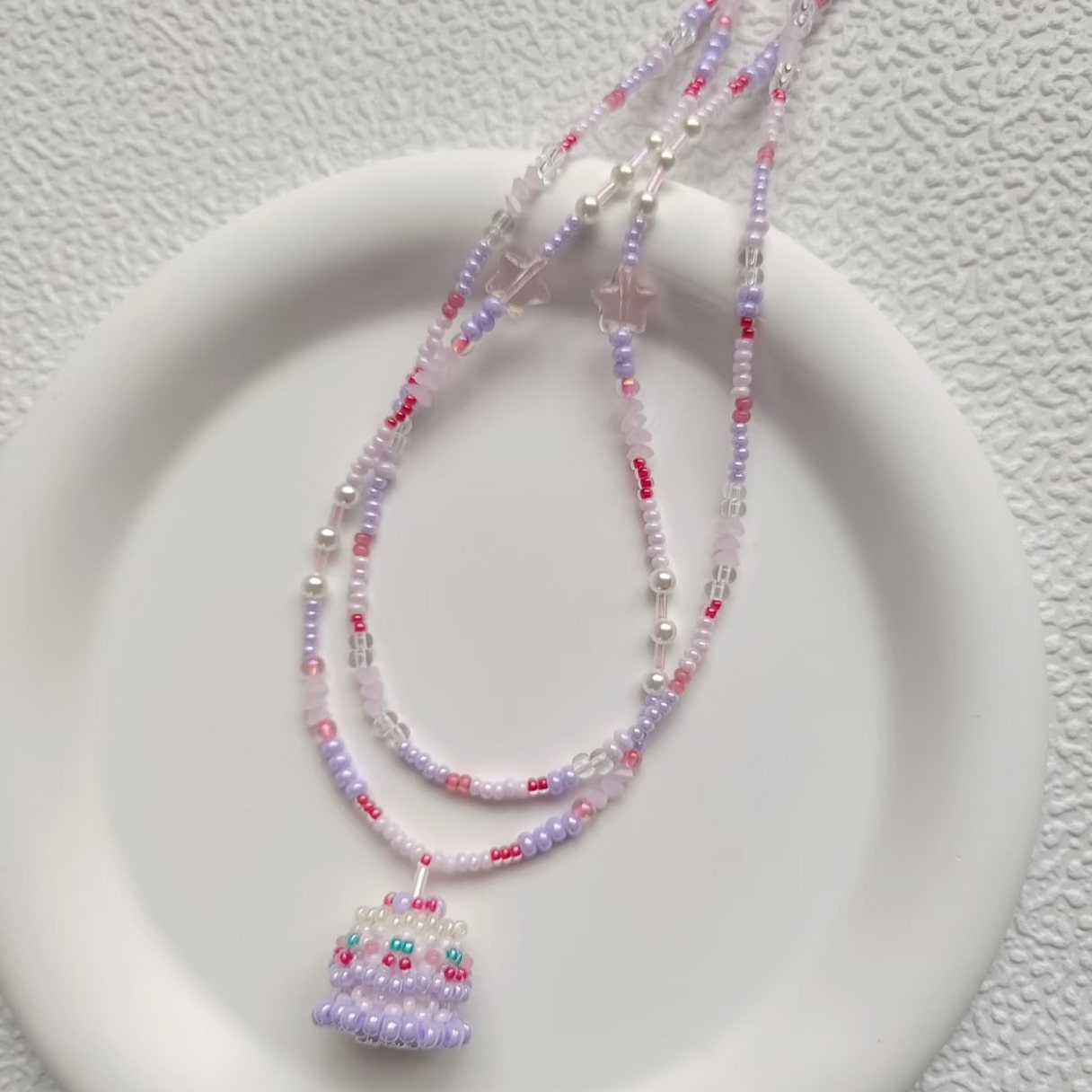 Beaded necklace with a cake pendant on a textured white surface