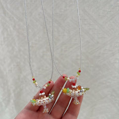Hand holding two small pudding boat cake necklaces with beads against a neutral background