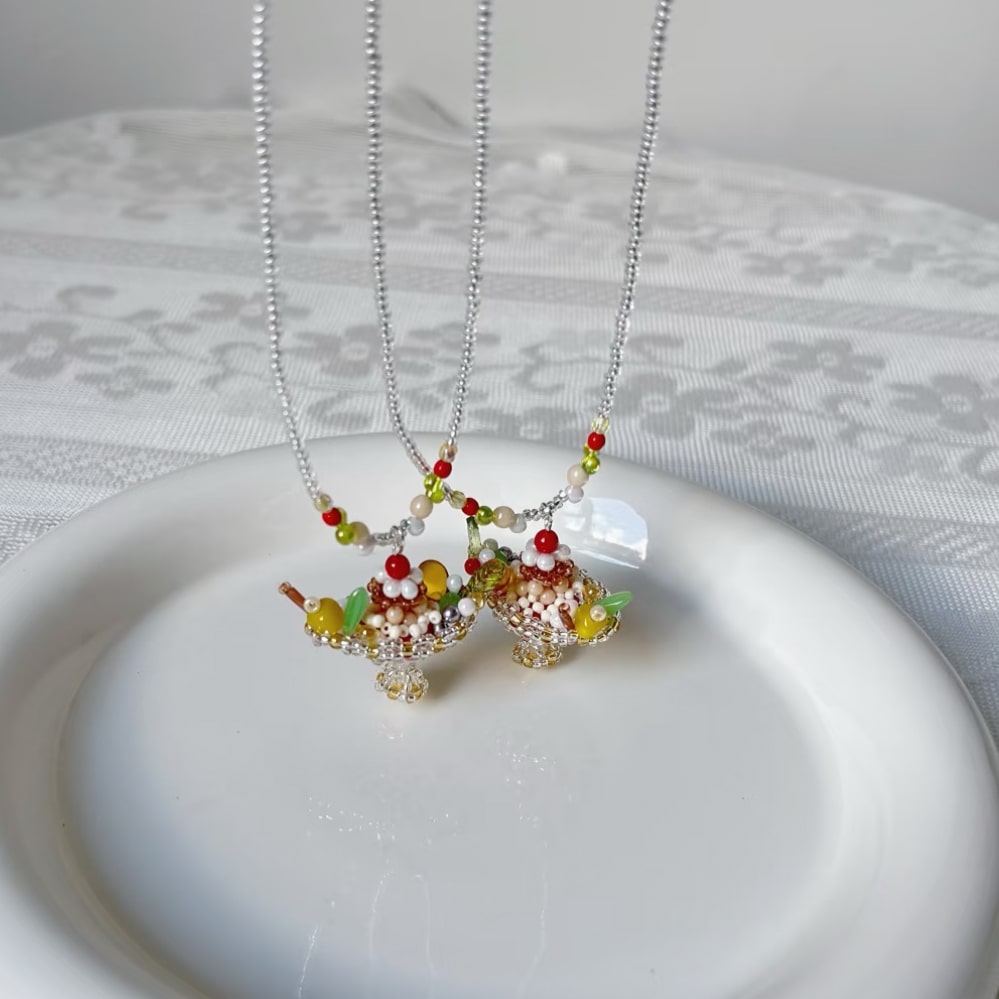 Two necklaces with colorful pudding boat cake pendant on a white plate