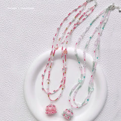 beaded birthday cake necklaces with pink and green pendants on a textured white surface