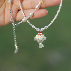 Necklace with a beaded pendant held by a hand against a blurred green background