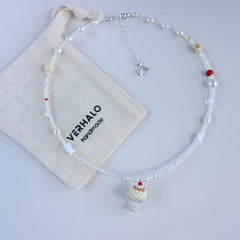 Beaded necklace with decorative pendants on a white background, featuring a Ver Halo branded pouch.