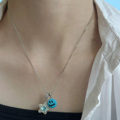 Necklace with a blue emoji pendant and star-shaped charm worn by a person.