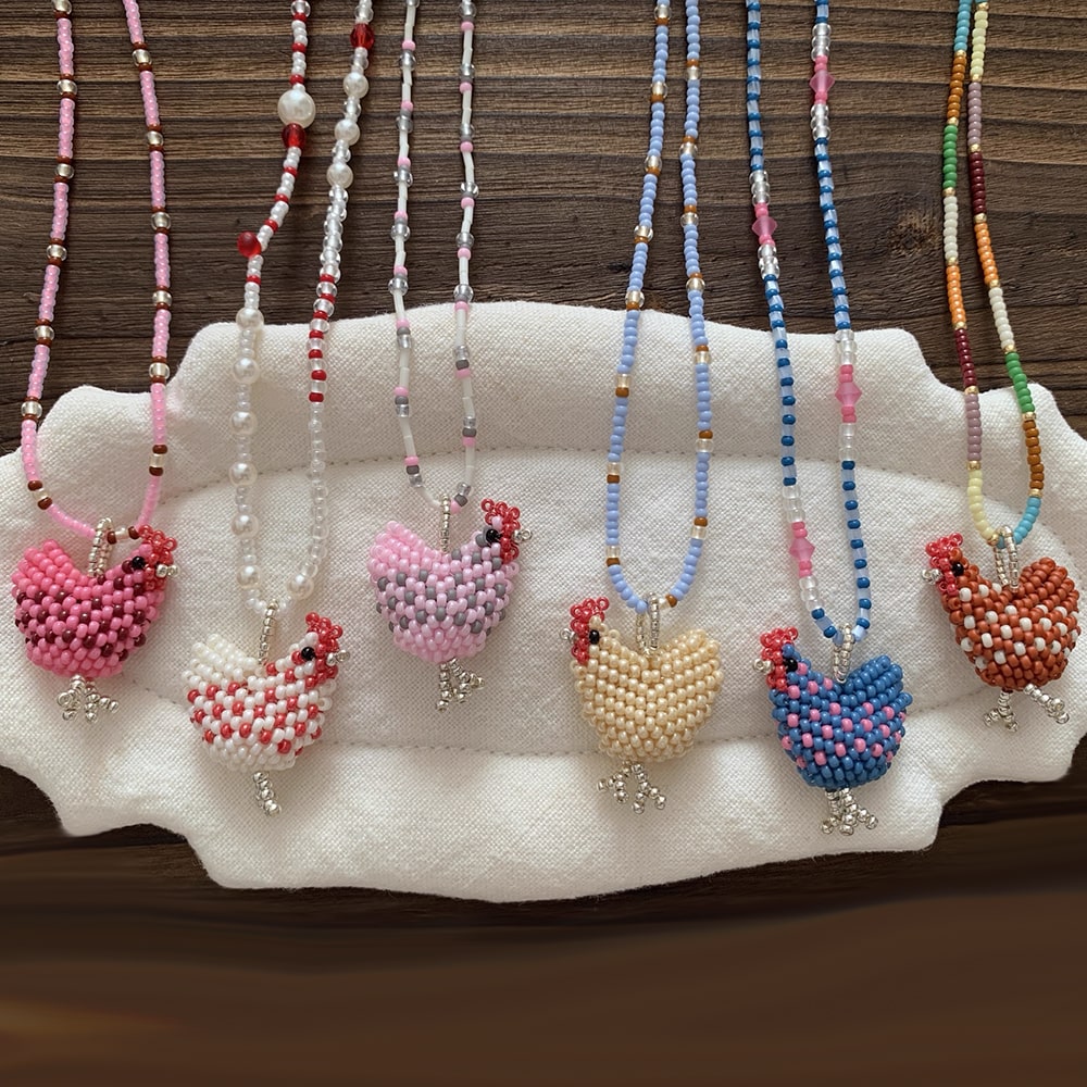 Colorful beaded necklaces with chicken-shaped pendants on a white stand against a wooden background. - Verhalo Jewelry