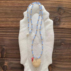 Beaded necklace with a white chicken charm on a mannequin hand against a wooden background - Verhalo Jewelry