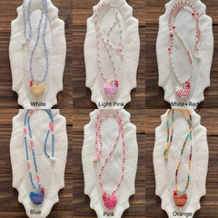 Set of beaded chicken necklaces on white stands with color labels on a wooden surface - Verhalo Jewelry