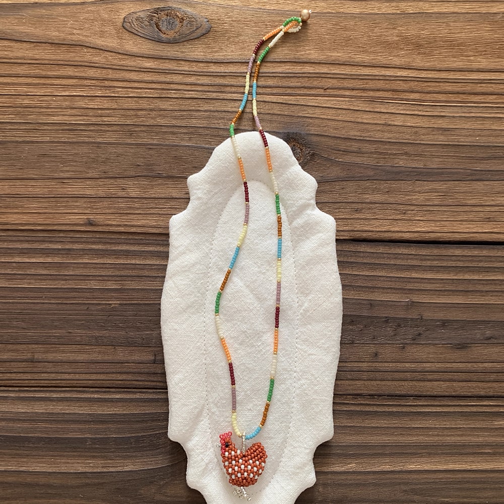 Necklace with orange chicken on a white stone surface against a wooden background - Verhalo Jewelry