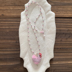 Beaded necklace with a pink chicken pendant on a textured white surface with a wooden background - Verhalo Jewelry