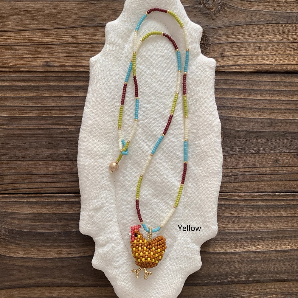 Beaded necklace with a yellow chicken pendant on a textured white surface with a wooden background. - Verhalo Jewelry