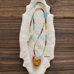 Beaded necklace with a yellow chicken pendant on a textured white surface with a wooden background. - Verhalo Jewelry