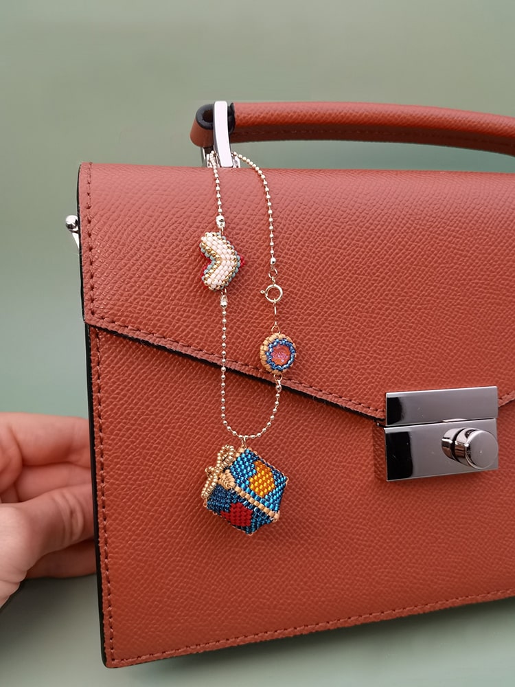 Brown handbag with colorful beaded gift box charm on a light green background