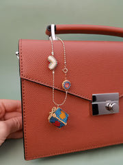 Brown handbag with colorful beaded gift box charm on a light green background