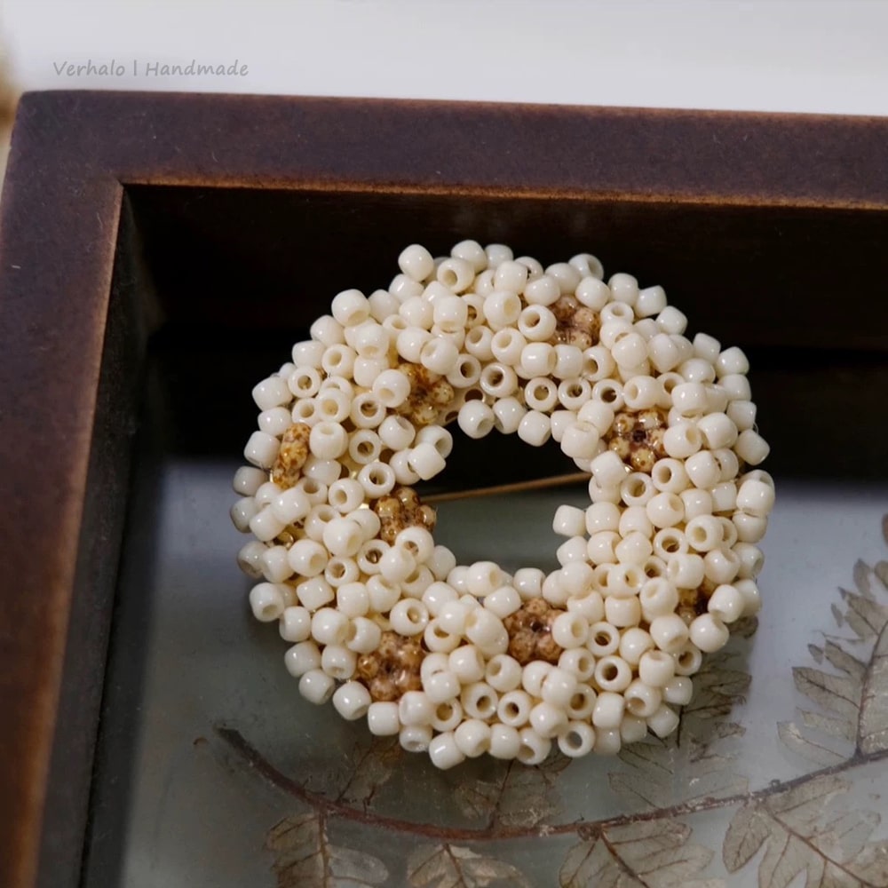 Beaded circular brooch on a textured surface with a wooden frame