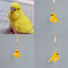 Yellow parakeet next to two yellow bird-shaped charms on a gray background