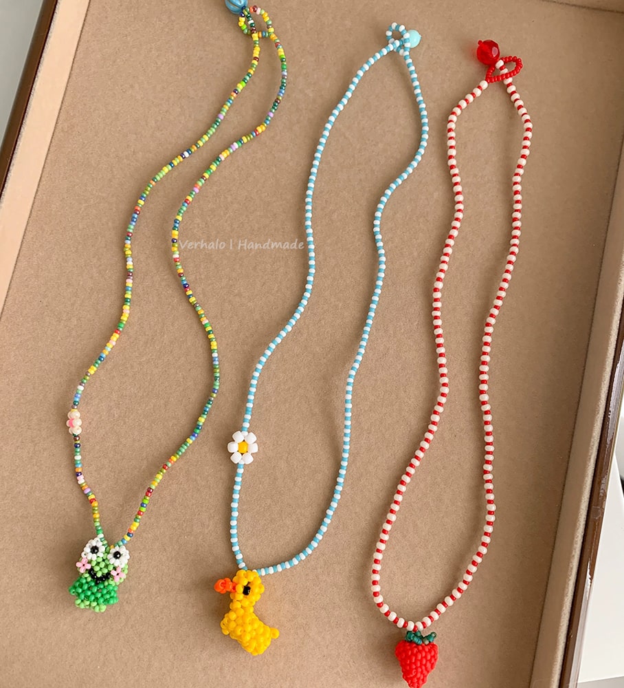 Three colorful beaded necklaces with small charm pendants on a brown background