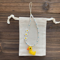 Beaded necklace with a yellow duck charm on a white pouch against a wooden background