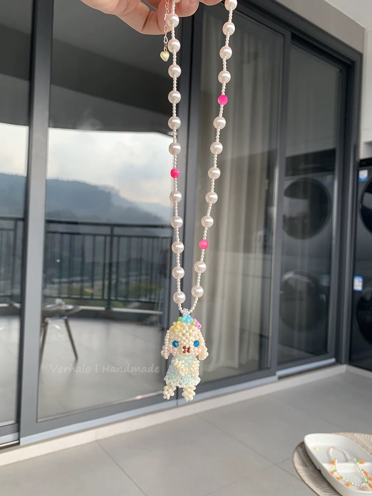 Holland Lop Necklace with beads and a small figurine held in front of a glass door.