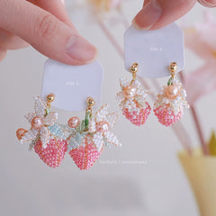 Strawberry-shaped earrings with pink and gold details on a white card.