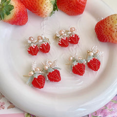 Strawberry-themed earrings on a white plate with strawberries