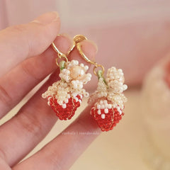 Handmade strawberry-shaped earrings held by a hand with a blurred background