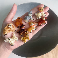 Hand holding small beaded dog figurines on a neutral background