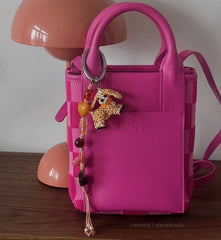 Pink bag with a keychain featuring a small figurine on a wooden surface.