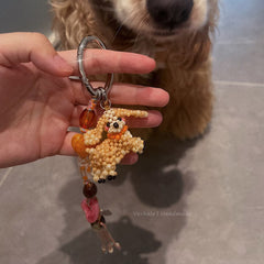 Hand holding a beaded keychain shaped like a dog with a dog in the background