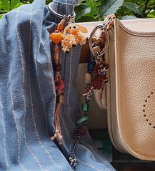 Colorful keychain with charms hanging from a blue denim jacket next to a beige handbag.
